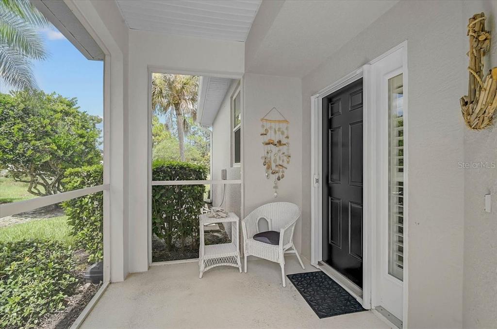 A screened-in porch features a black front door, white wicker furniture, and a shell mobile — 1631 MONARCH DRIVE UNIT 1631, VENICE, FL
