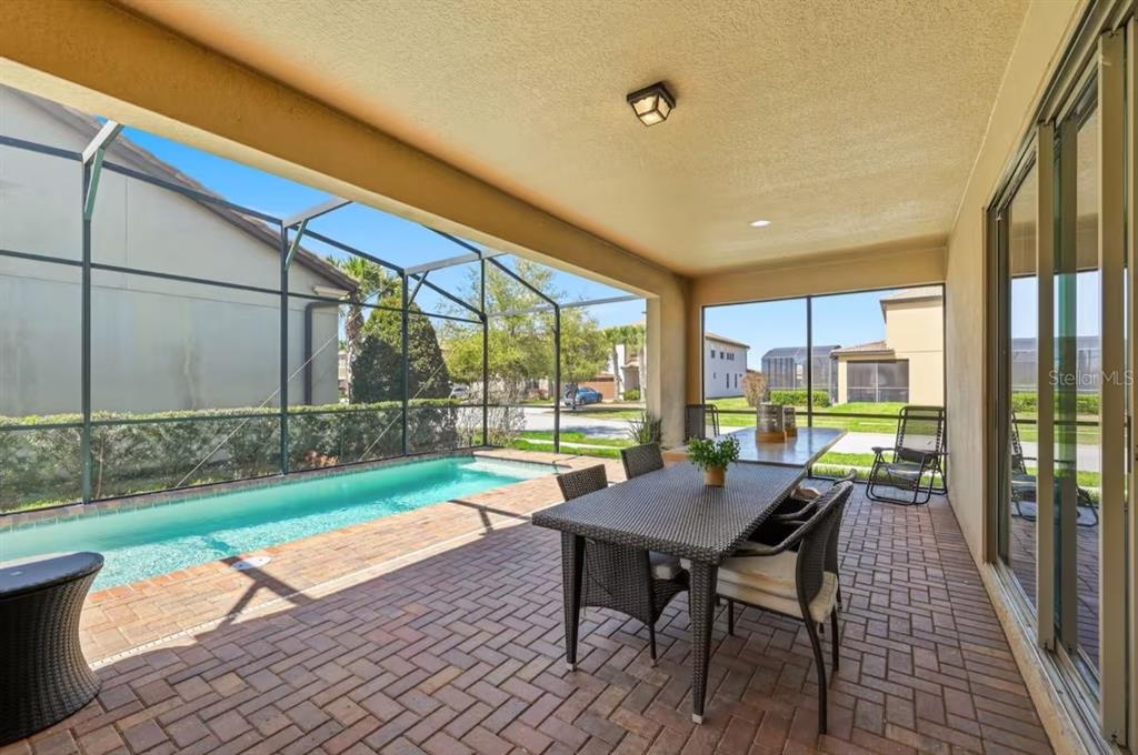 A covered patio features a brick floor, a dining set, and an adjacent swimming pool — 1836 NICE COURT, KISSIMMEE, FL