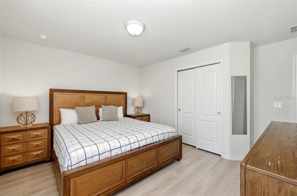 A bedroom features a wooden bed frame, matching nightstands, light flooring, and a white closet — 1836 NICE COURT, KISSIMMEE, FL