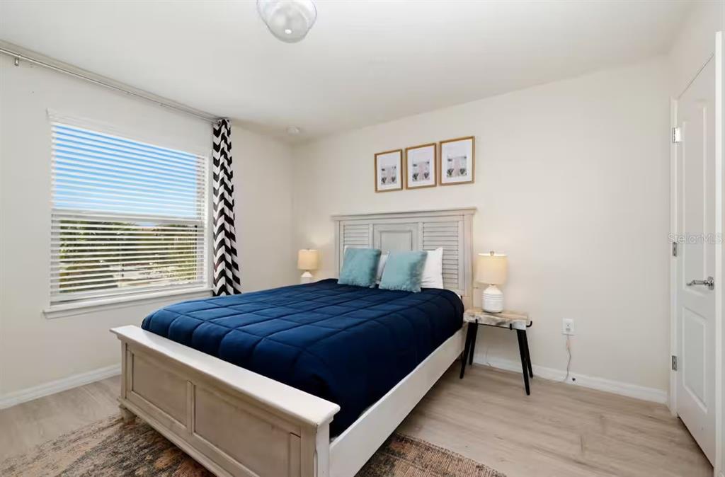 A bedroom features a bed with a blue quilt, light wood flooring, and three wall frames — 1836 NICE COURT, KISSIMMEE, FL