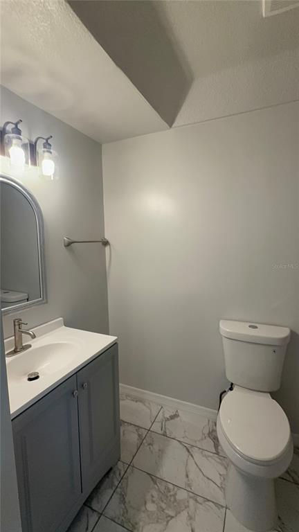 A bathroom features a gray vanity, a white toilet, and white marble-patterned tile flooring — 2218 AVENUE B SW, WINTER HAVEN, FL