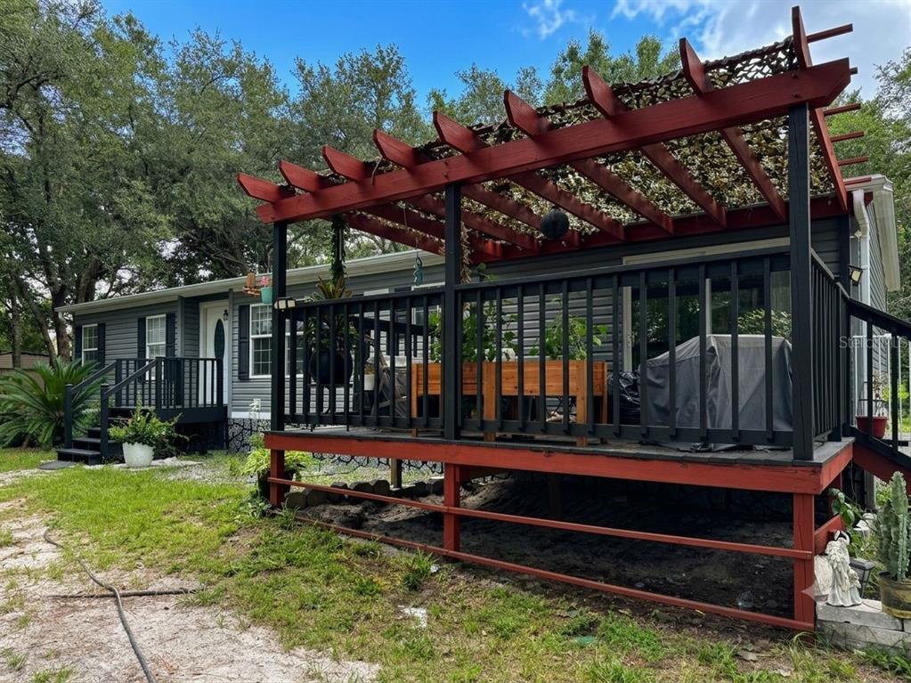 A gray house features a large wooden deck with a red pergola and black railings — 7495 SW 155TH STREET, DUNNELLON, FL