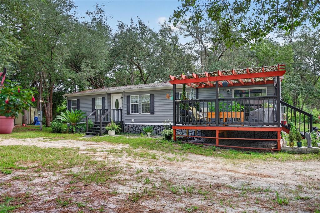 A gray manufactured home features a large red-framed deck with a pergola and lattice roof — 7495 SW 155TH STREET, DUNNELLON, FL