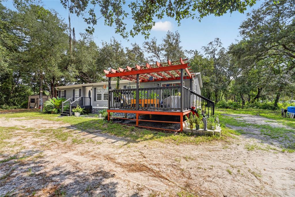 A single-story house with a red pergola over a wooden deck in a wooded yard — 7495 SW 155TH STREET, DUNNELLON, FL