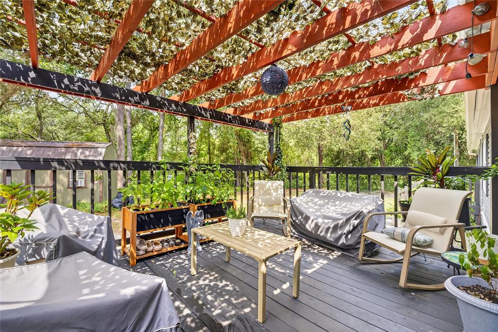 A wooden deck features a pergola with artificial greenery, outdoor furniture, and potted plants — 7495 SW 155TH STREET, DUNNELLON, FL