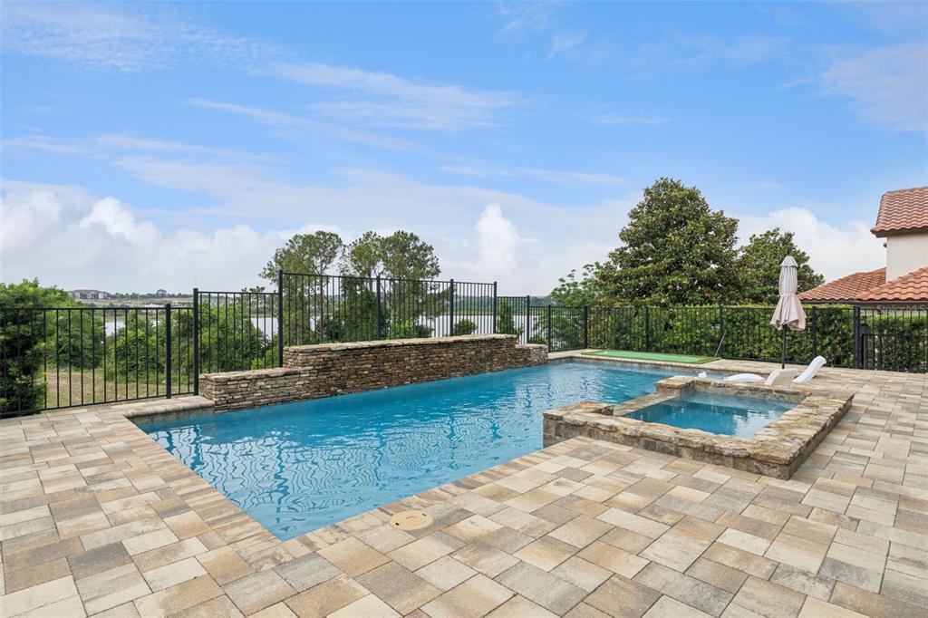 A backyard swimming pool and spa with stone accents overlook a lake behind a fence — 1784 BELLA LAGO DRIVE, CLERMONT, FL