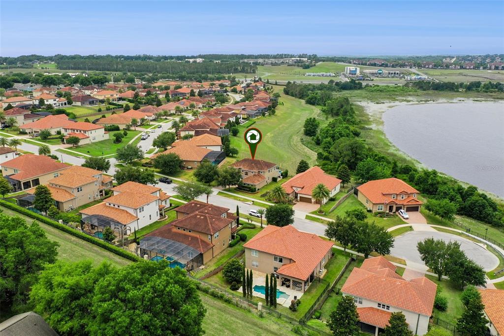 An aerial view shows a suburban neighborhood with houses, a lake, and green spaces — 1784 BELLA LAGO DRIVE, CLERMONT, FL