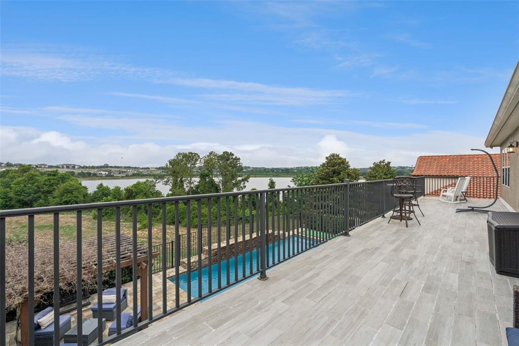 An elevated outdoor deck overlooks a swimming pool and a lake under a blue sky — 1784 BELLA LAGO DRIVE, CLERMONT, FL