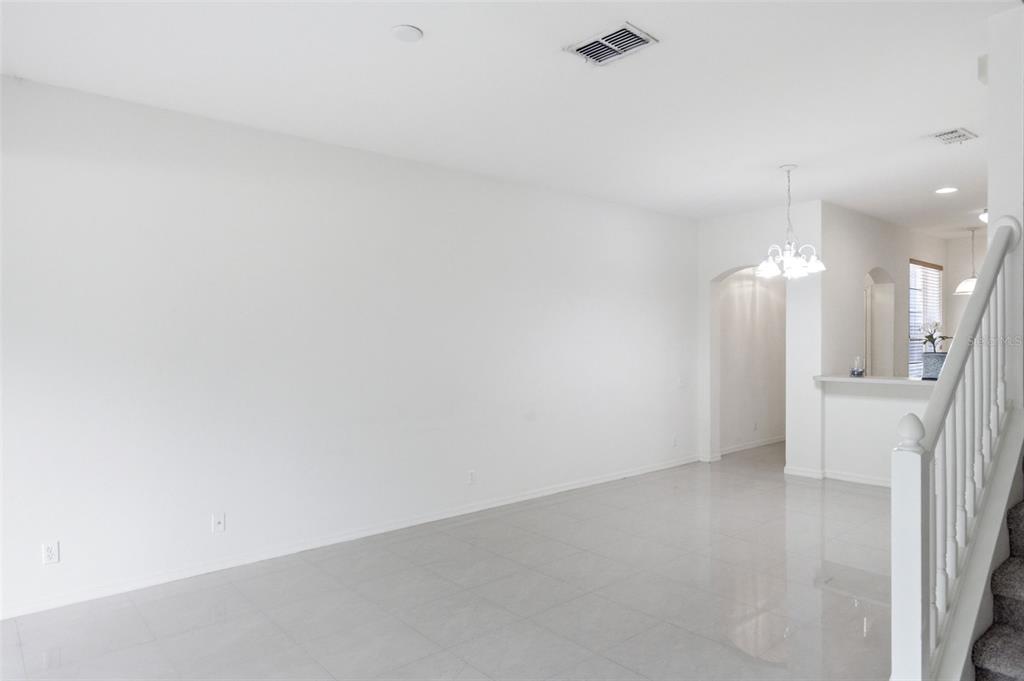 A bright, empty living room with white walls, light tile flooring, and a staircase — 4132 BISMARCK PALM DRIVE, TAMPA, FL