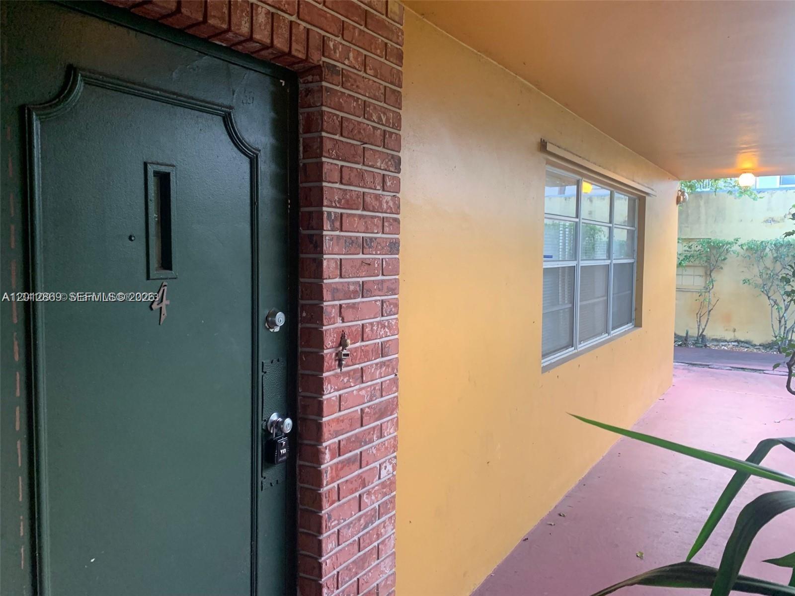 A green door with a brick surround sits next to a yellow wall and window — 1702 Mckinley St # 4, Hollywood FL 33020, HOLLYWOOD, FL