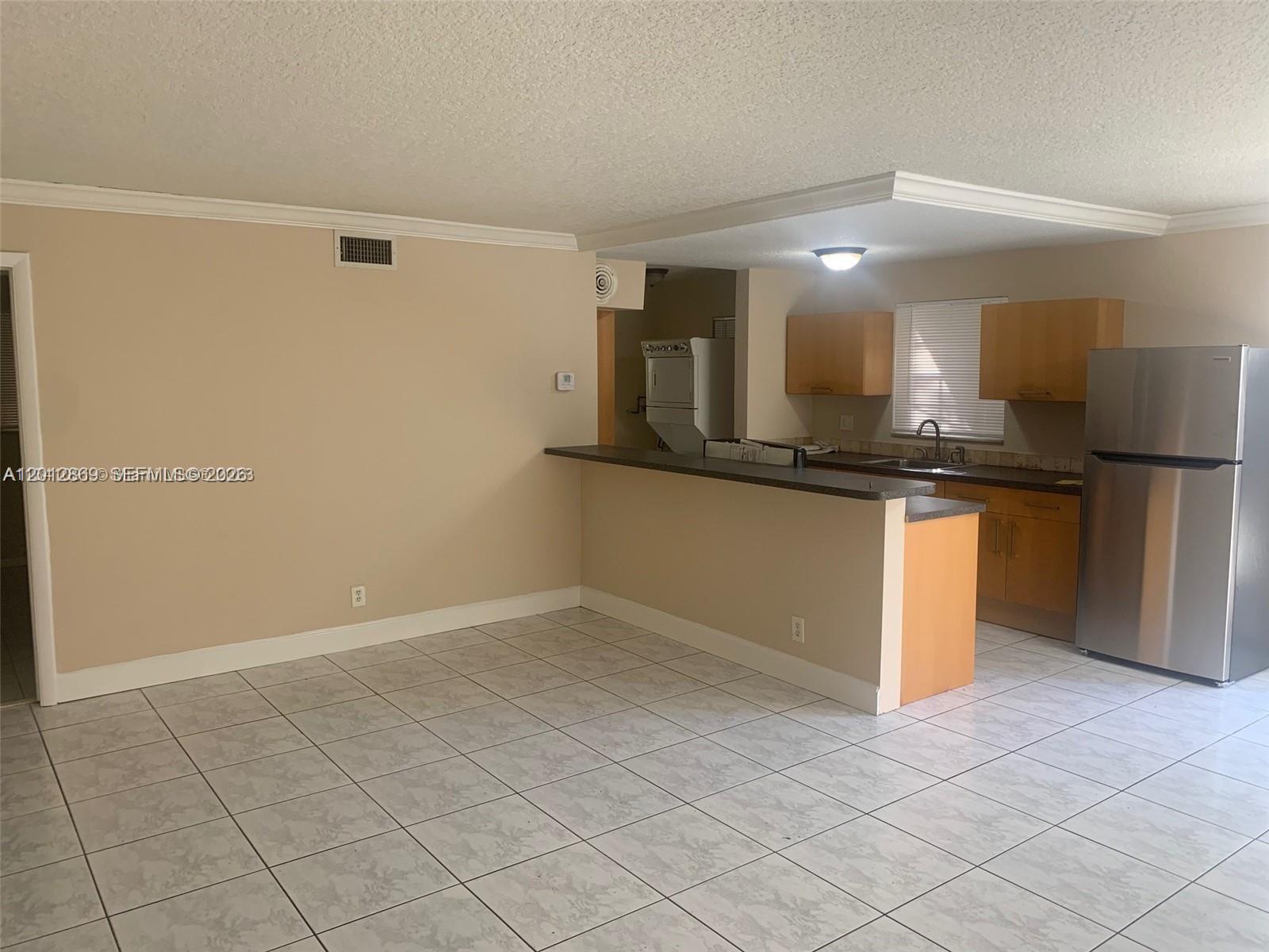 A kitchen with light wood cabinets, stainless steel appliances, and tile flooring opens to a living area — 1702 Mckinley St # 4, Hollywood FL 33020, HOLLYWOOD, FL