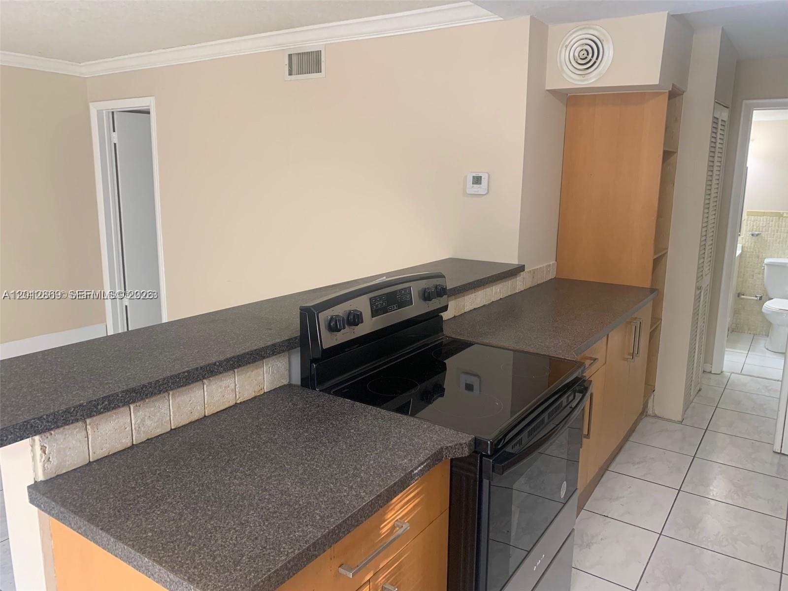 A kitchen features dark countertops, light wood cabinets, a black electric stove, and tiled floors — 1702 Mckinley St # 4, Hollywood FL 33020, HOLLYWOOD, FL