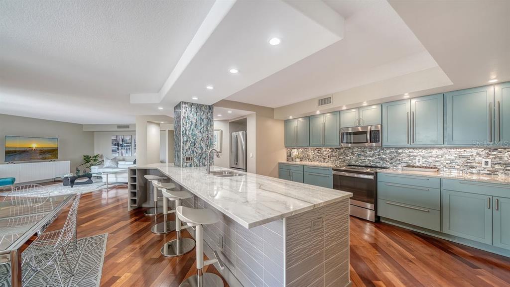 A modern kitchen features light blue cabinets, a marble island with bar seating, and hardwood floors — 1111 N GULFSTREAM AVENUE UNIT 4E, SARASOTA, FL