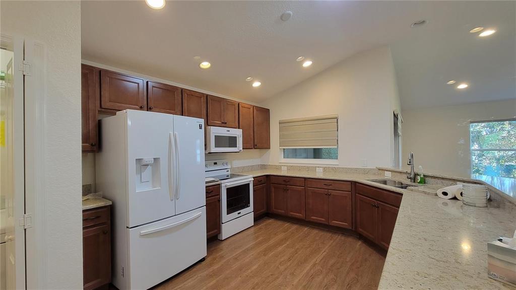A kitchen features wood cabinets, granite countertops, white appliances, and a vaulted ceiling — 4992 SANDPIPER DRIVE, OXFORD, FL