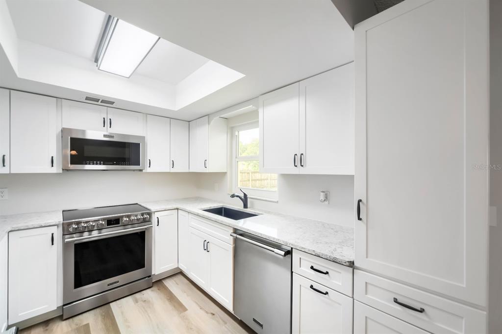 A modern kitchen features white cabinets, stainless steel appliances, granite countertops, and a skylight — 3432 UNITY TREE DRIVE, EDGEWATER, FL