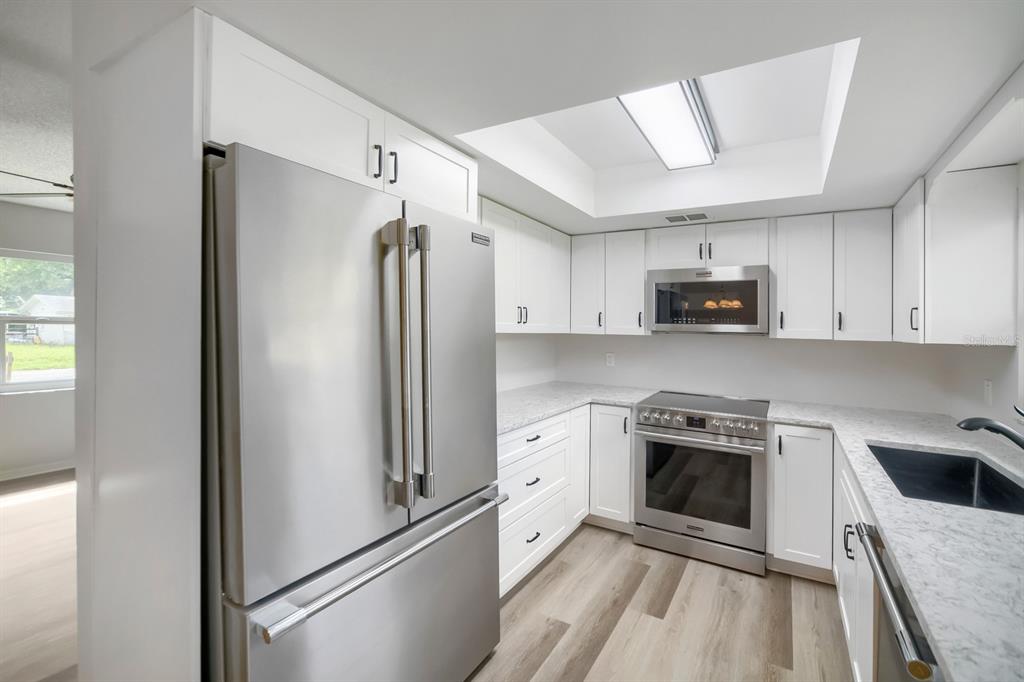 A modern kitchen features white cabinets, stainless steel appliances, and light-colored countertops — 3432 UNITY TREE DRIVE, EDGEWATER, FL