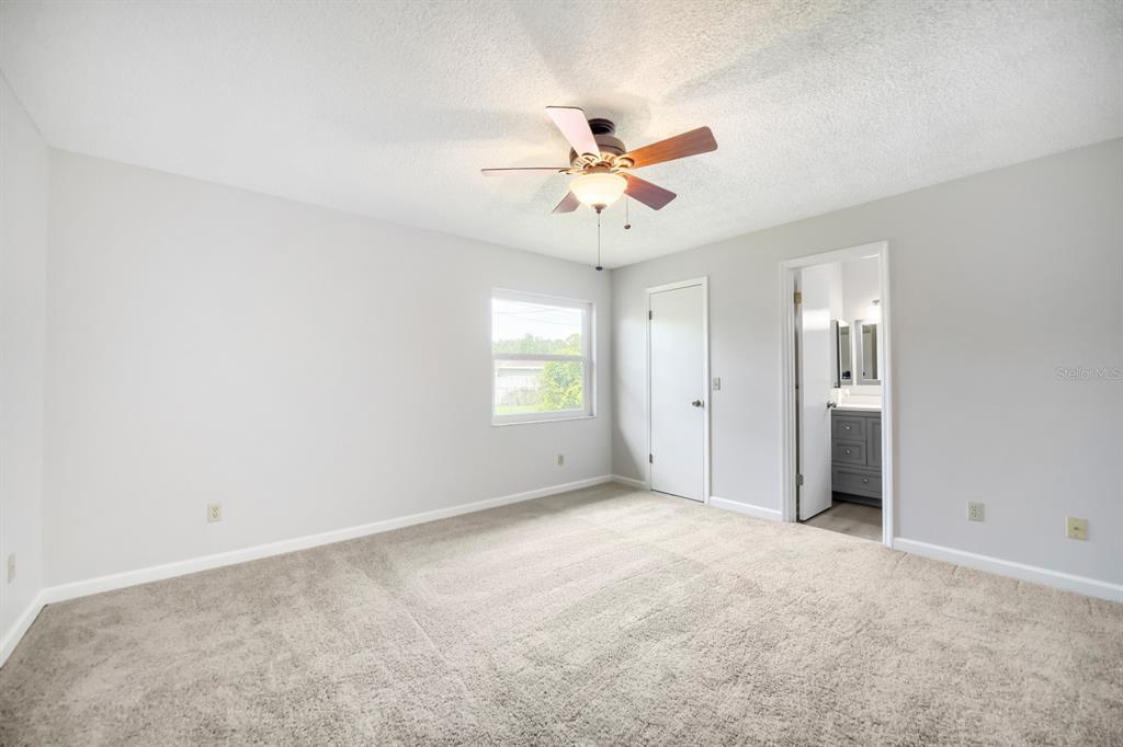 A bedroom with light gray walls, beige carpeting, a ceiling fan, and an attached bathroom — 3432 UNITY TREE DRIVE, EDGEWATER, FL
