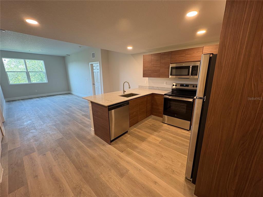 A kitchen with wood-tone cabinets and stainless steel appliances opens to a living area — 4424 S TEXAS AVENUE UNIT 1-305, ORLANDO, FL