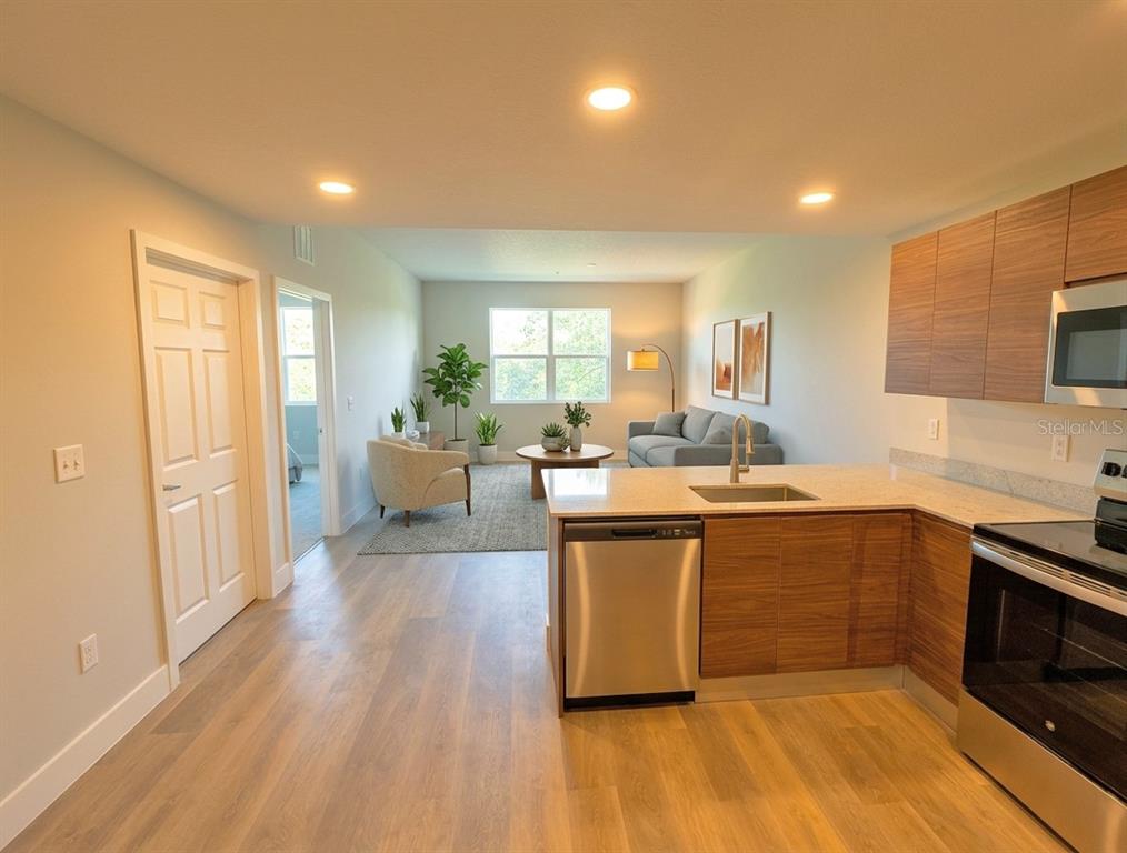 A kitchen with wood-toned cabinets and stainless steel appliances overlooks an open-concept living area — 4424 S TEXAS AVENUE UNIT 1-305, ORLANDO, FL
