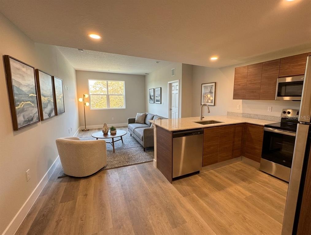 An open-concept living room and kitchen featuring wood-look flooring, modern cabinetry, and stainless steel appliances — 4424 S TEXAS AVENUE UNIT 1-305, ORLANDO, FL