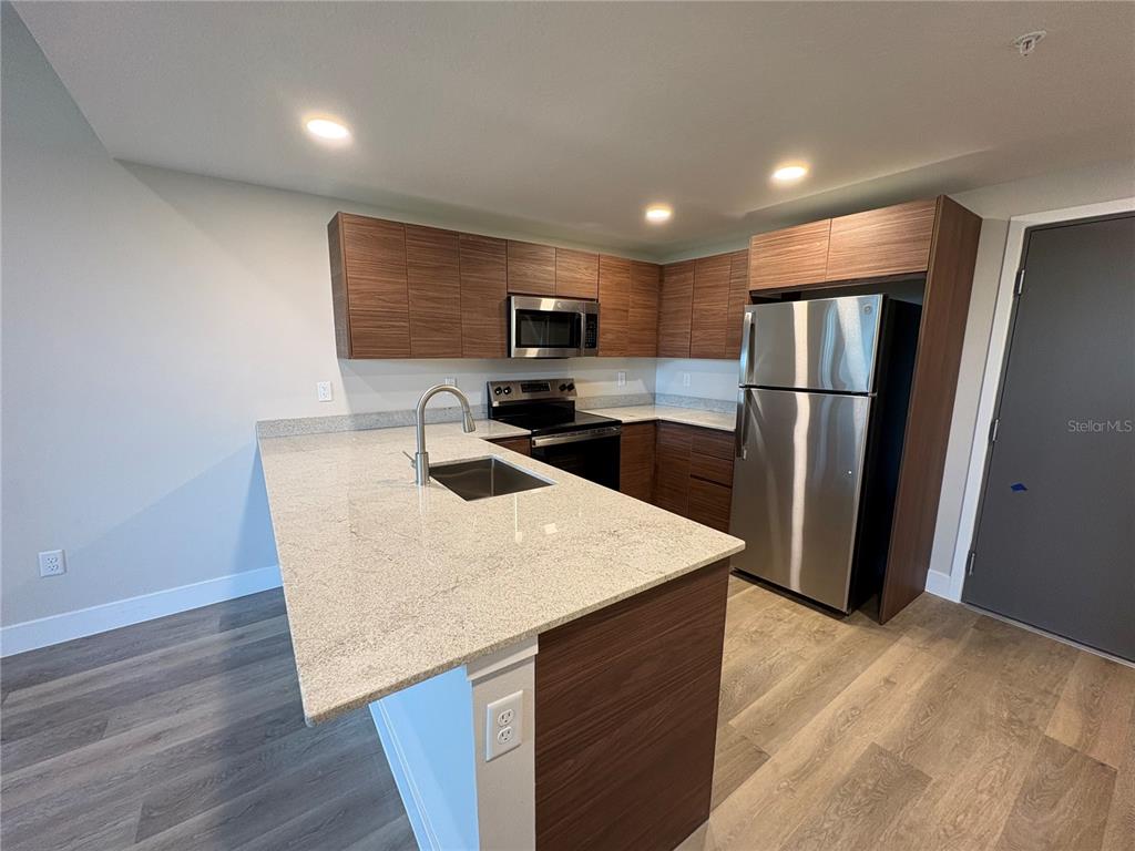 A modern kitchen features wood-grain cabinets, stainless steel appliances, and a granite-topped island — 4424 S TEXAS AVENUE UNIT 1-305, ORLANDO, FL