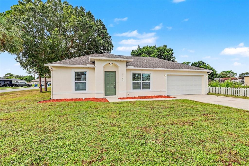 A single-story house with a beige stucco exterior, a green front door, and a two-car garage — 1142 JASLO STREET SE, PALM BAY, FL