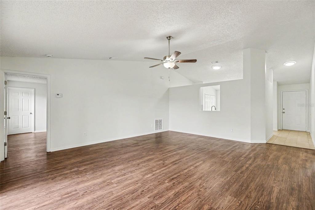 An empty living room with wood-look flooring, white walls, a ceiling fan, and a doorway — 1142 JASLO STREET SE, PALM BAY, FL