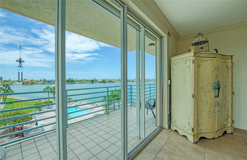 A balcony with a view of a pool and water, seen through sliding glass doors — 7974 SAILBOAT KEY BOULEVARD S UNIT 301, SOUTH PASADENA, FL