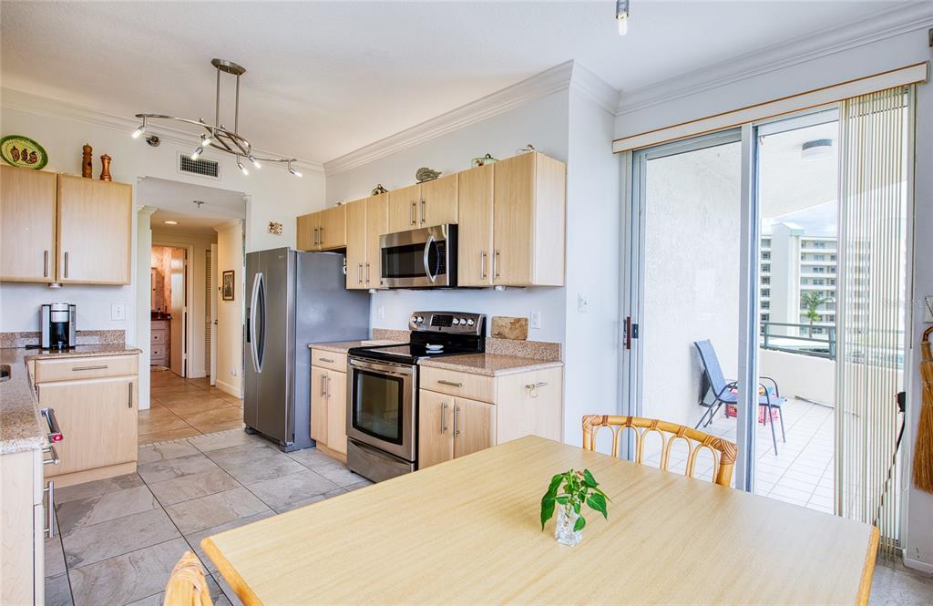 A kitchen with light wood cabinets, stainless steel appliances, and a dining area near a balcony — 7974 SAILBOAT KEY BOULEVARD S UNIT 301, SOUTH PASADENA, FL