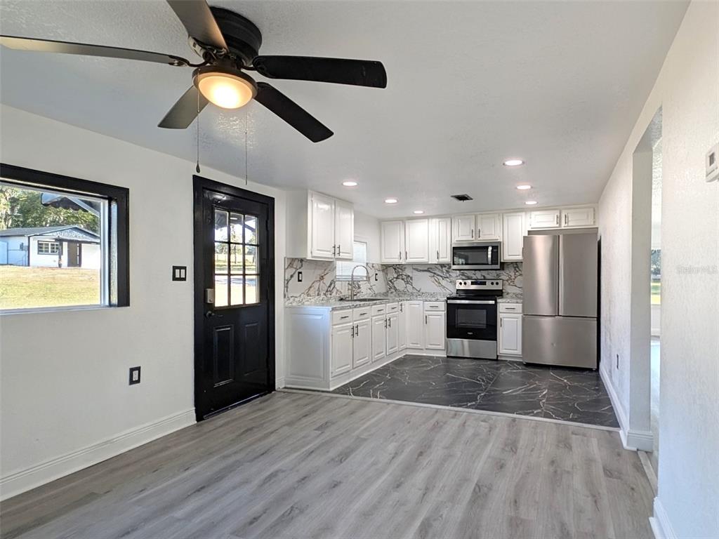 A kitchen features white cabinets, marble-patterned backsplashes, stainless steel appliances, and a black-tiled floor area — 15209 BAILEY HILL ROAD, BROOKSVILLE, FL