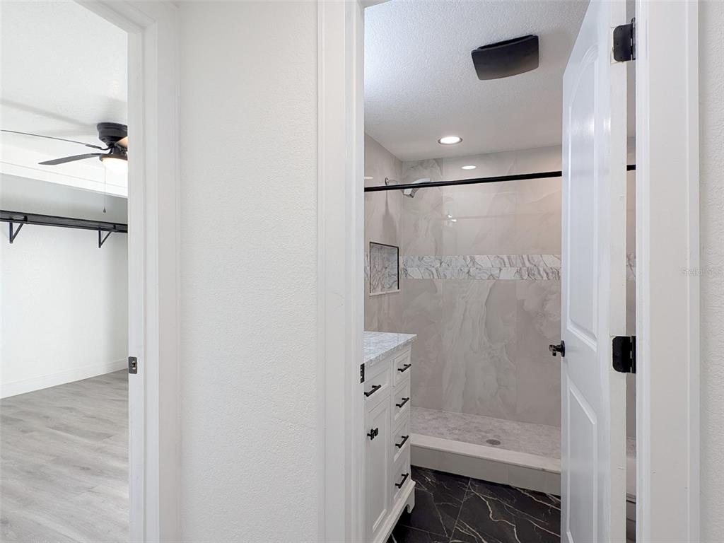 A bathroom with a white vanity and a tiled walk-in shower viewed through a doorway — 15209 BAILEY HILL ROAD, BROOKSVILLE, FL