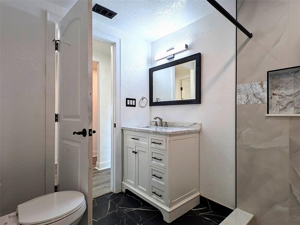 A bathroom features a white vanity with a marble top, black-framed mirror, and tiled shower — 15209 BAILEY HILL ROAD, BROOKSVILLE, FL