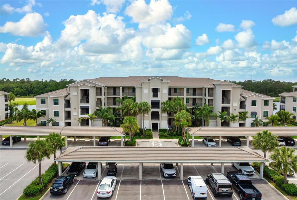 An aerial view of a multi-story apartment building with covered parking spaces in the foreground — 17704 GAWTHROP DRIVE UNIT 205, BRADENTON, FL