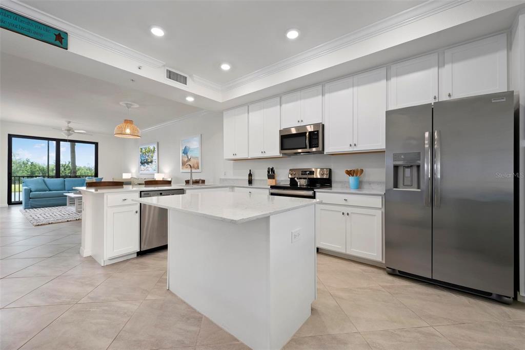 A modern kitchen features white cabinetry, stainless steel appliances, and a central island with countertops — 17704 GAWTHROP DRIVE UNIT 205, BRADENTON, FL