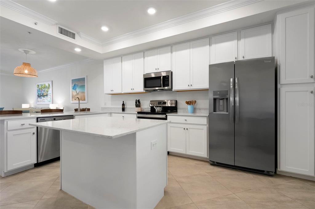 A modern kitchen features white cabinetry, stainless steel appliances, a quartz island, and tile flooring — 17704 GAWTHROP DRIVE UNIT 205, BRADENTON, FL