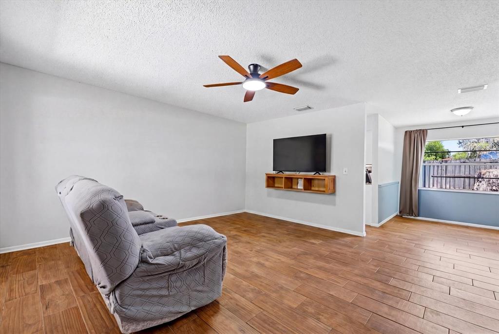 A living room features wood-look tile flooring, a ceiling fan, and a wall-mounted television — 2429 MARTHA LANE, LAND O LAKES, FL