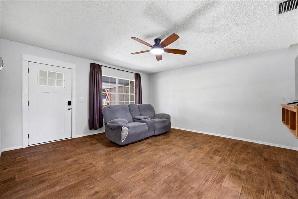 A living room features wood-look tile flooring, a gray loveseat, and a ceiling fan — 2429 MARTHA LANE, LAND O LAKES, FL