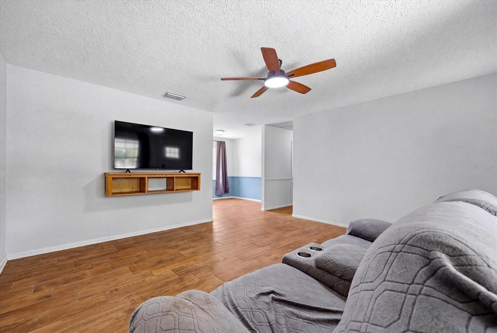 A living room features a wall-mounted television, wood-look tile flooring, and a ceiling fan — 2429 MARTHA LANE, LAND O LAKES, FL