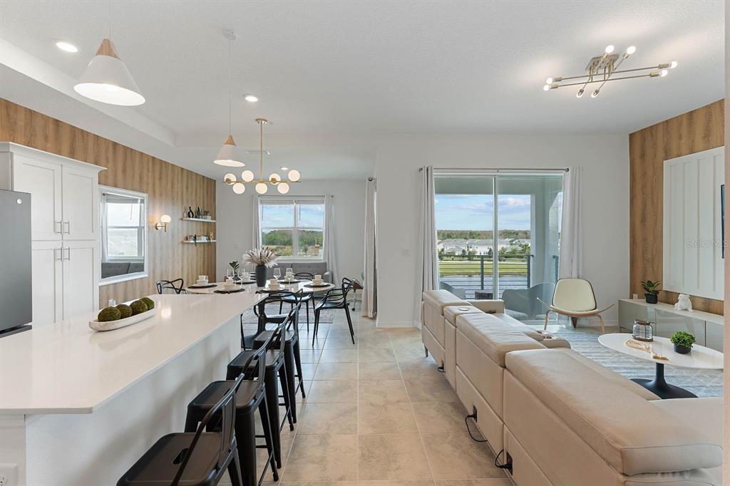 An open-concept kitchen and living area features a white island, wood-paneled walls, and sliding doors — 3191 PARADOX CIRCLE UNIT 405, KISSIMMEE, FL