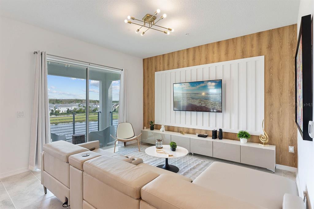 A living room features a wood-paneled accent wall, a wall-mounted television, and a sliding glass door — 3191 PARADOX CIRCLE UNIT 405, KISSIMMEE, FL