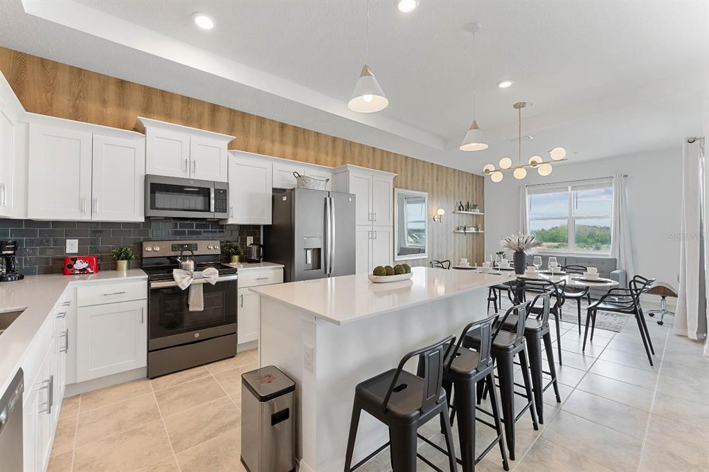 A modern kitchen features white cabinetry, a large island with bar stools, and wood-paneled walls — 3191 PARADOX CIRCLE UNIT 405, KISSIMMEE, FL