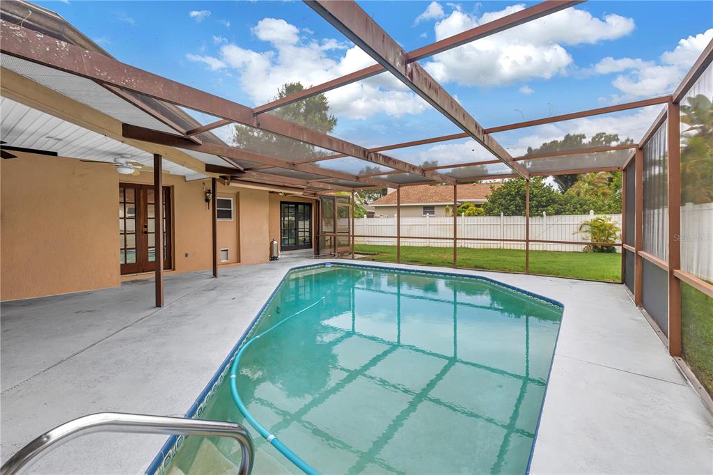 A swimming pool sits on a concrete patio enclosed by a screened-in lanai structure — 9212 RUSTIC PINES BOULEVARD W, SEMINOLE, FL