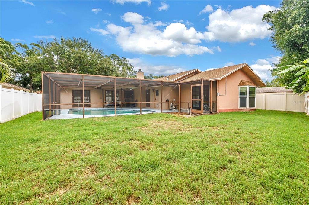 The backyard features a swimming pool enclosed by a screen cage and a grassy lawn — 9212 RUSTIC PINES BOULEVARD W, SEMINOLE, FL