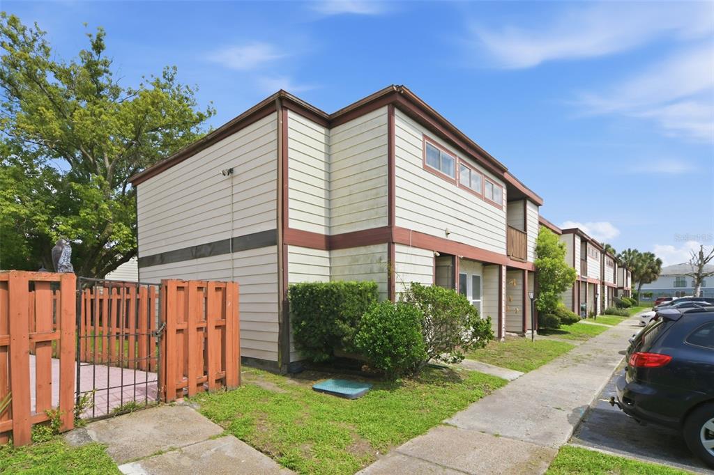 An exterior view of a two-story apartment building with light siding and a fenced patio — 4001 DOLOMITE STREET UNIT B1, ORLANDO, FL