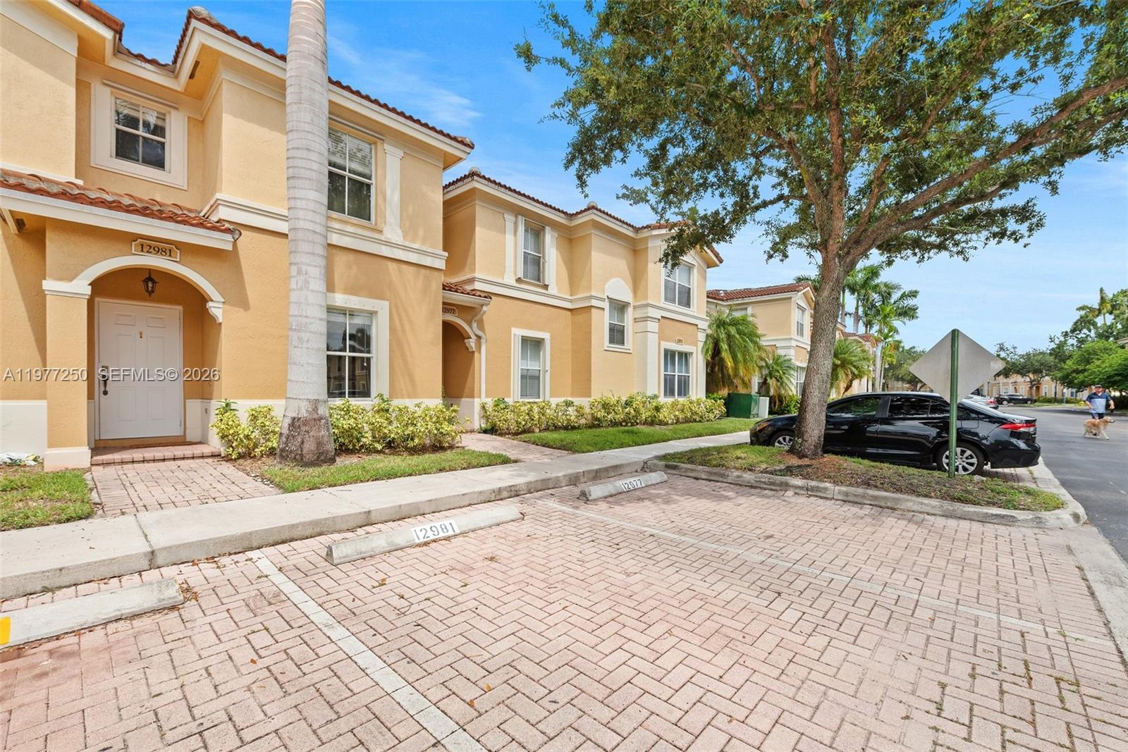 A row of two-story tan stucco townhomes features brick-paved parking spaces in front — 12981 SW 30th St, Miramar FL 33027, MIRAMAR, FL