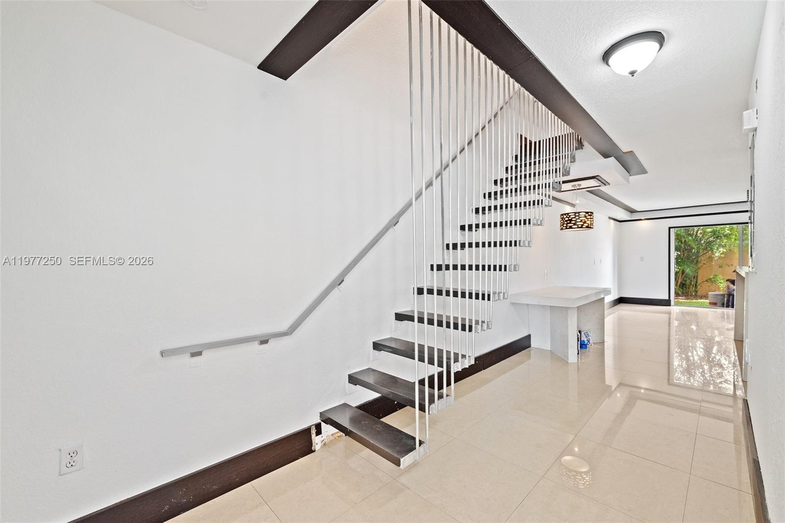 A modern staircase with dark treads and metal railings stands in a bright, tiled room — 12981 SW 30th St, Miramar FL 33027, MIRAMAR, FL