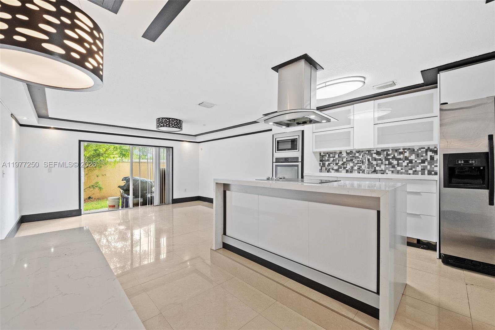 A modern kitchen features a white island, stainless steel appliances, and a sliding glass door — 12981 SW 30th St, Miramar FL 33027, MIRAMAR, FL