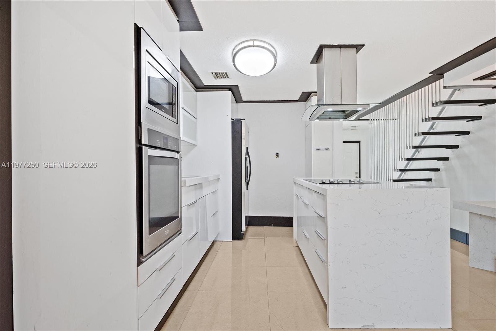 A modern kitchen features white cabinetry, a marble-topped island, stainless steel appliances, and a staircase — 12981 SW 30th St, Miramar FL 33027, MIRAMAR, FL