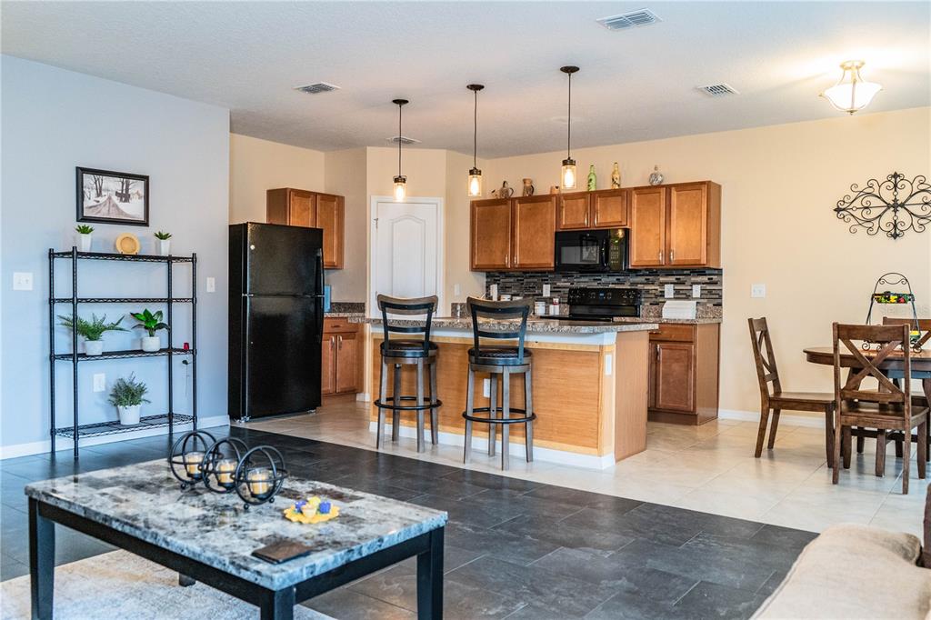 An open-concept kitchen features wood cabinets, granite countertops, and a breakfast bar with stools — 256 OLEANDER STREET, WINTER HAVEN, FL