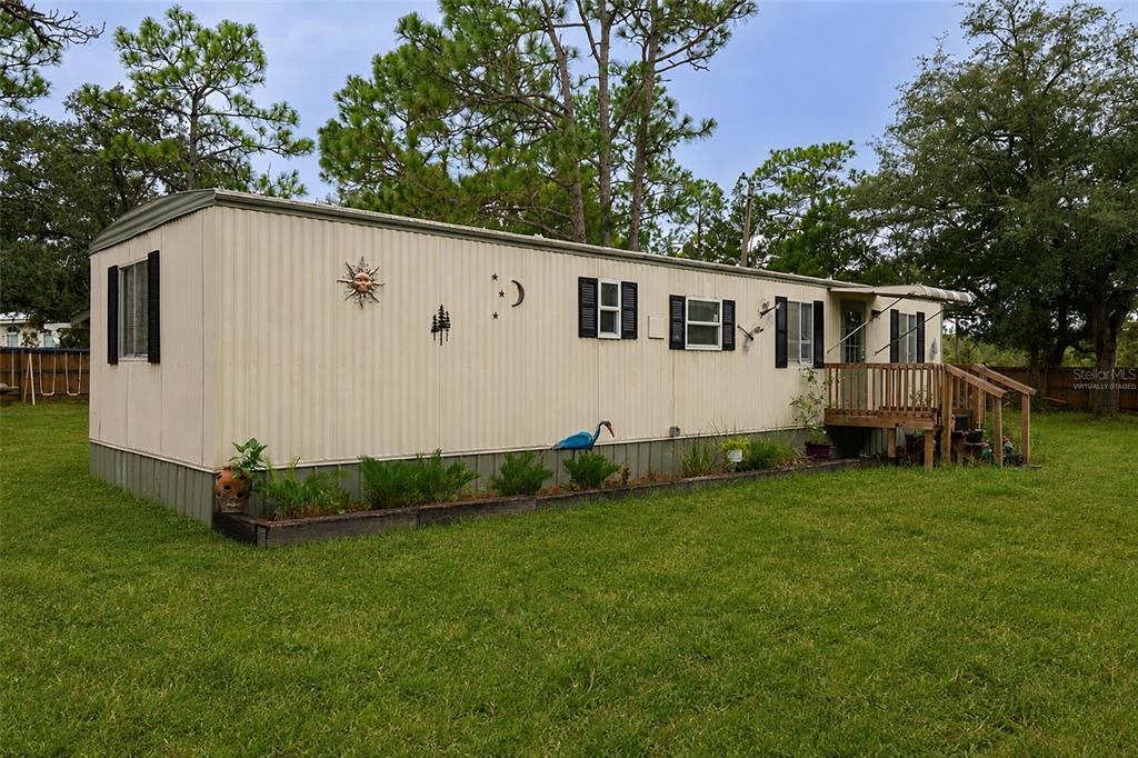 A single-story mobile home with tan siding and a small wooden deck sits on grass — 5108 W FIELD STREET, HOMOSASSA, FL